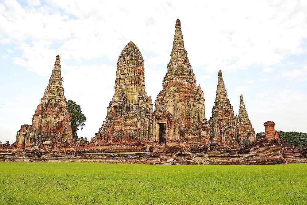 Scenic view of the historical wat chaiwatthanaram temple with its towering prangs and serene green lawn under a cloudy sky in ayutthaya, thailand