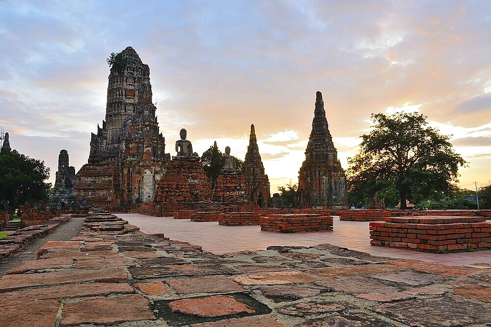 Serene buddha statues sit amidst crumbling temple ruins, bathed in the golden light of a beautiful sunset in thailand