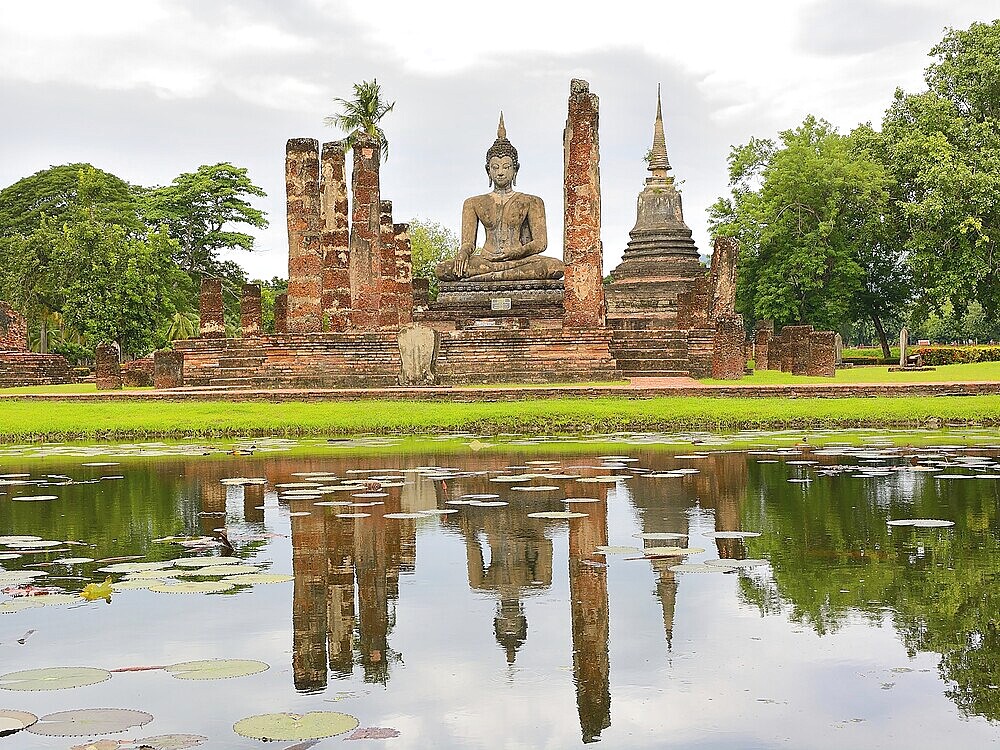 Serene buddha statue reflected in a pond at the sukhothai historical park, a unesco world heritage site in thailand