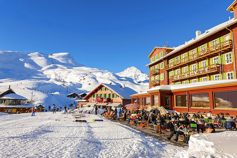 The Famous and Historical Hotel Bellevue des Alpes with People on the Terrace at 2061 Meters High Up and Mountain Peak with Ski Slope in a Sunny Winter Day in Kleine Scheidegg, Grindelwald, Bern Canton, Switzerland