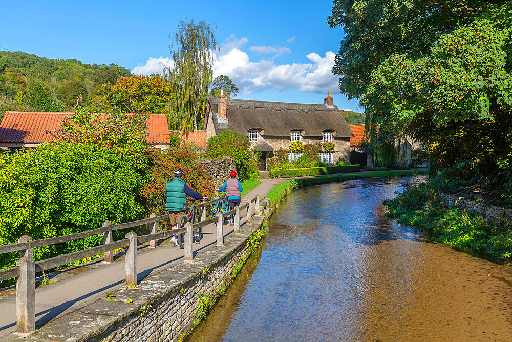 View of cyclists, riverside thatched cottage and Thornton Beck, Thornton Dale, North Yorkshire, England, United Kingdom, Europe