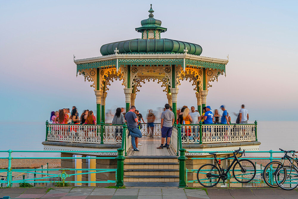 View of people on ornate bandstand on sea front at dusk, Brighton, East Sussex, England, United Kingdom, Europe