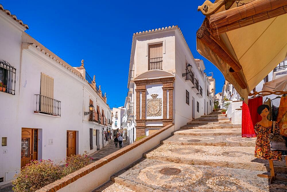 View of white washed houses and clothes shop on narrow street, Frigiliana, Malaga Province, Andalucia, Spain, Europe