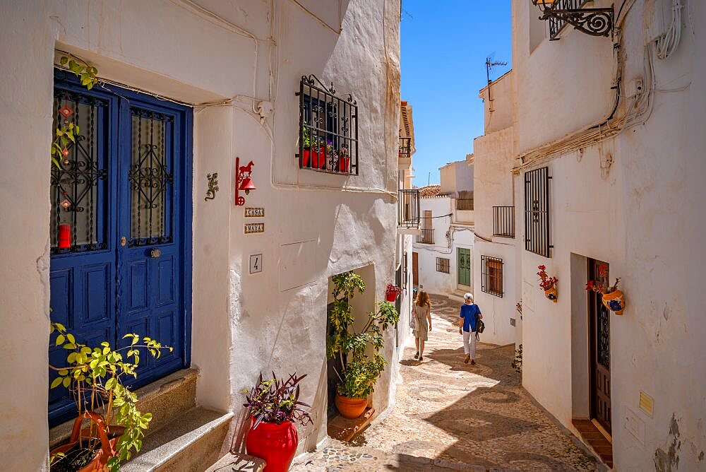 View of ladies walking through narrow street of white washed houses, Frigiliana, Malaga Province, Andalucia, Spain, Europe