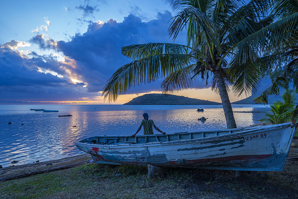 View of local man sat on boat viewing Le Morne from Le Morne Brabant at sunset, Savanne District, Mauritius, Indian Ocean, Africa