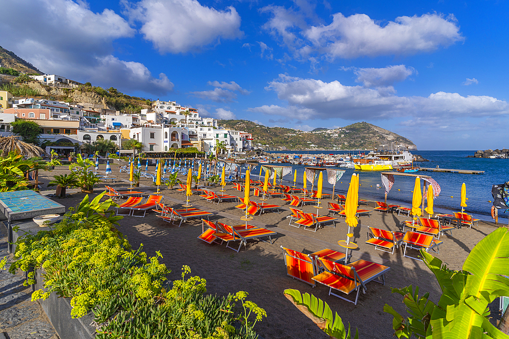 View of brightly coloured loungers on the beach and Sant'Angelo from Porto di Sant'Angelo, Sant'Angelo, Island of Ischia, Campania, Italy, Europe