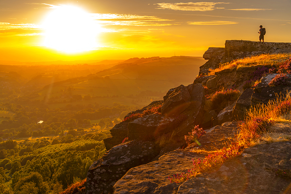 View of hiker viewing landsacpe from Curbar Edge at sunset, Peak District National Park, Baslow, Derbyshire, England, United Kingdom, Europe