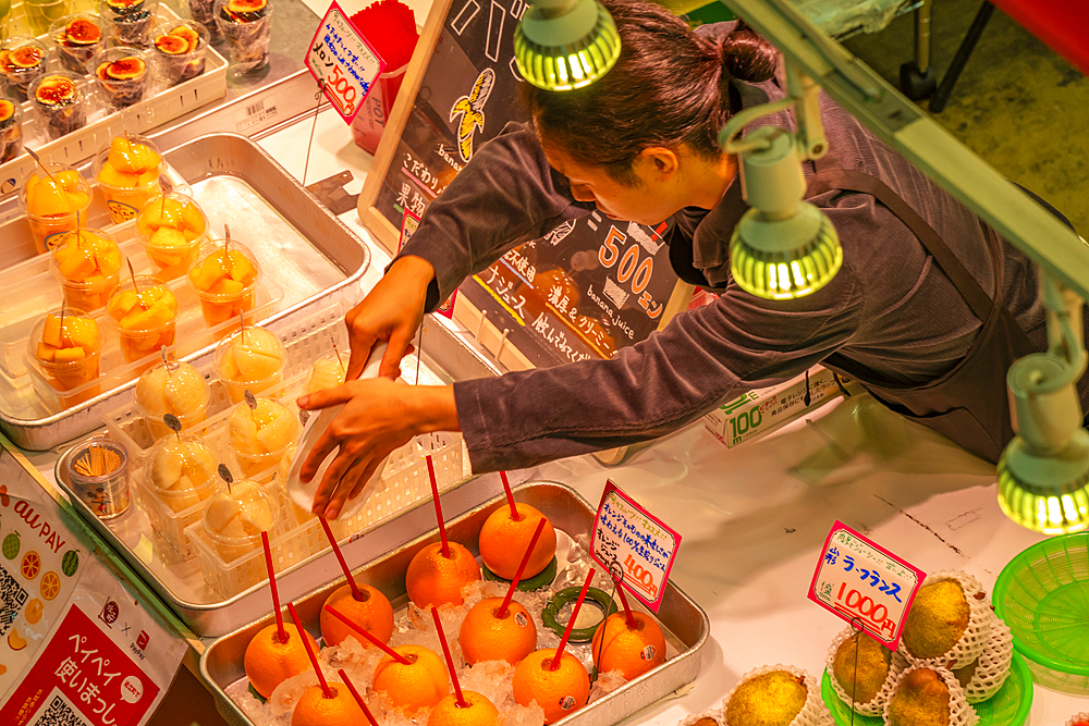 Elevated view of colourful fresh fruit stall and stall holder in Omicho Market, Kanazawa City, Ishikawa Prefecture, Honshu, Japan, Asia