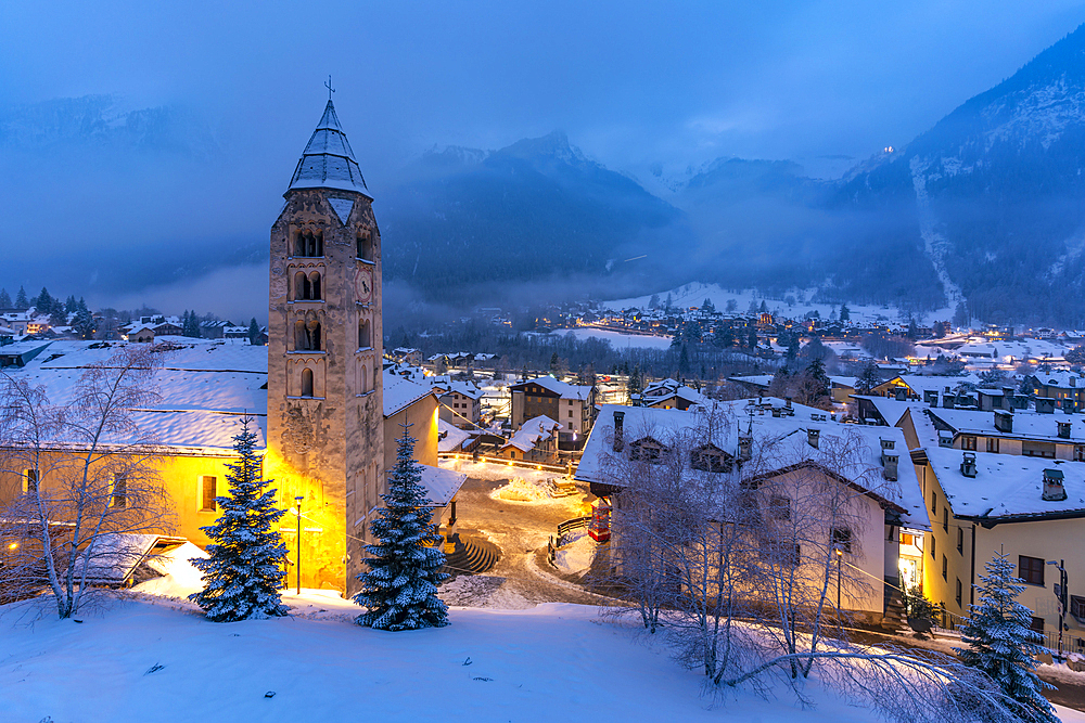 View of Church of Saint Pantalon and the snow covered town centre and mountainous background in winter at dusk, Courmayeur, Aosta Valley, Italy, Europe