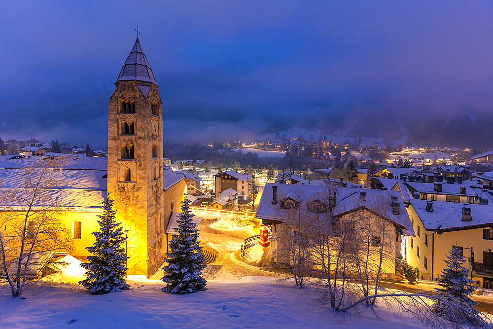 View of Church of Saint Pantalon and the snow covered town centre and mountainous background in winter at dusk, Courmayeur, Aosta Valley, Italy, Europe