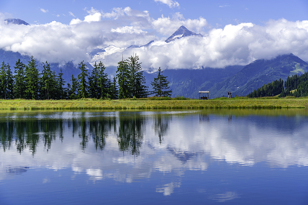 View of reflection of mountains and clouds in Plettsaukopf Reservoir on a sunny day, Bruckberg, Salzburg, Austria, Europe