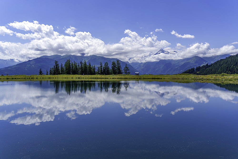 View of reflection of mountains and clouds in Plettsaukopf Reservoir on a sunny day, Bruckberg, Salzburg, Austria, Europe