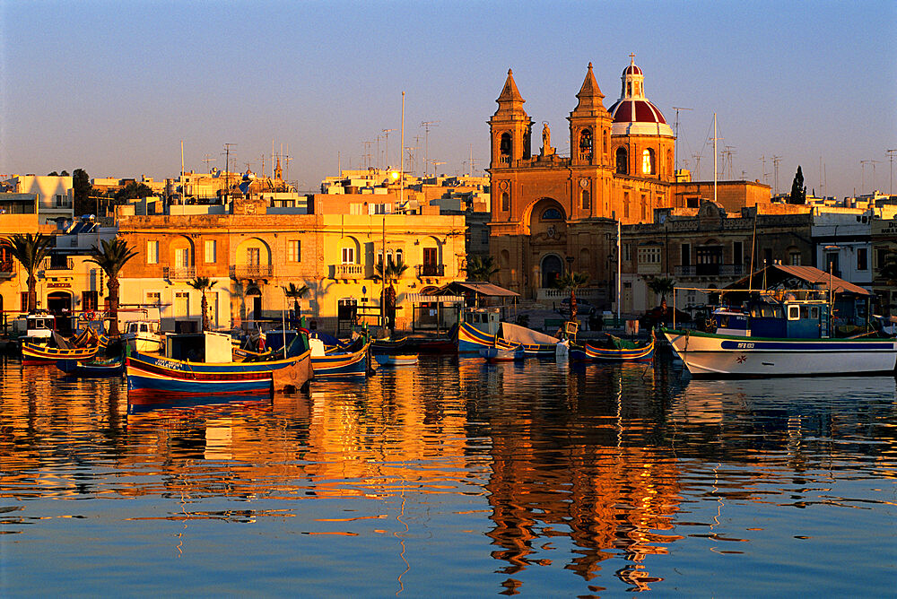 Harbour with Luzzu fishing boats and Marsaxlokk Parish Church at sunrise, Marsaxlokk, Malta, Mediterranean, Europe