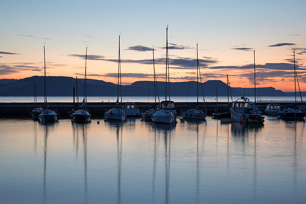 Yachts moored in The Cobb with Jurassic Coast and Golden Cap at sunrise, Lyme Regis, Dorset, England, United Kingdom, Europe