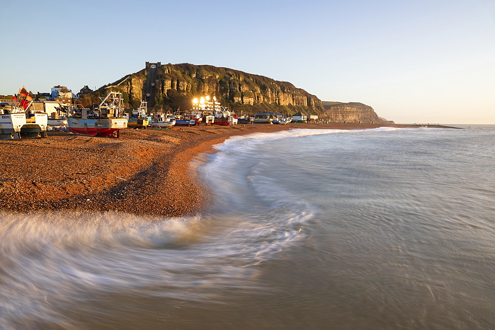 Fishing boats on beach at The Stade with breaking waves and East Hill behind at sunrise, Hastings, East Sussex, England, United Kingdom, Europe