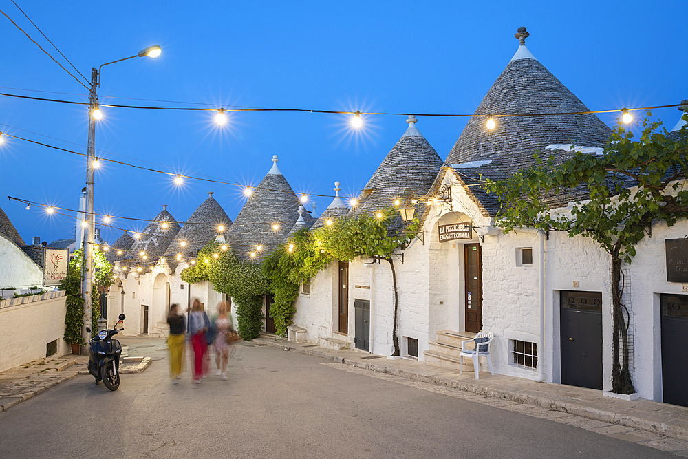 Whitewashed trulli houses along Via Monte San Michele street in the old town lit up at dusk, Alberobello, Puglia, Italy, Europe