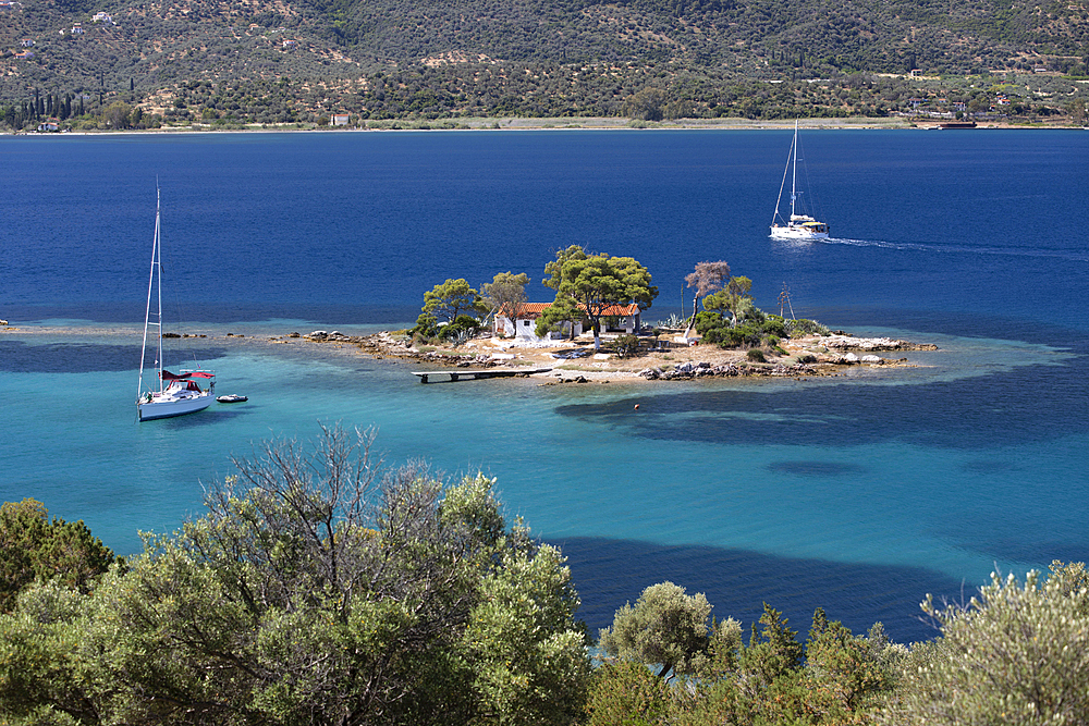 Greek Orthodox church on small island with anchored yacht off Russian Bay with crystal clear turquoise water, Poros, Saronic islands, Greek Islands, Greece, Europe