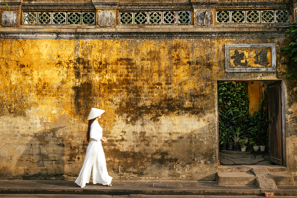 Vietnamese woman in ao dai walking past buildings, Hoi An, Quảng Nam Province, Vietnam
