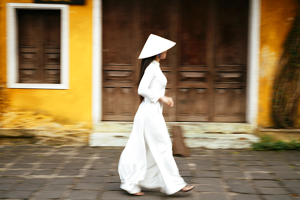 Vietnamese woman in ao dai walking past buildings, Hoi An, Quảng Nam Province, Vietnam
