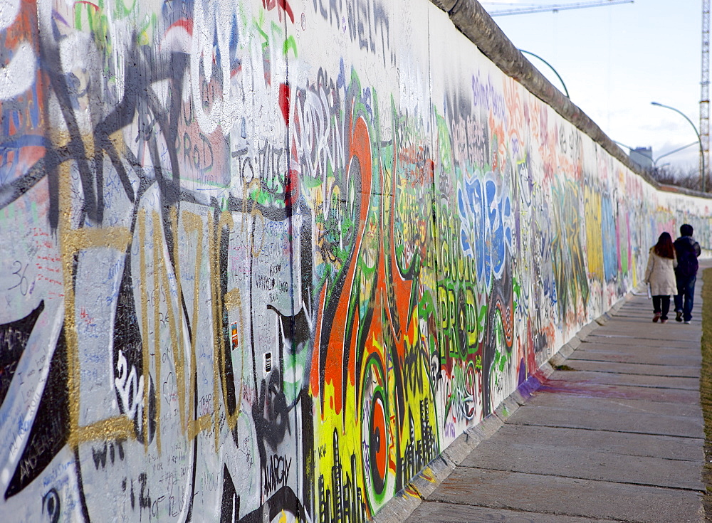 Couple walking along the East Side Gallery Berlin Wall mural, Berlin, Germany, Europe 