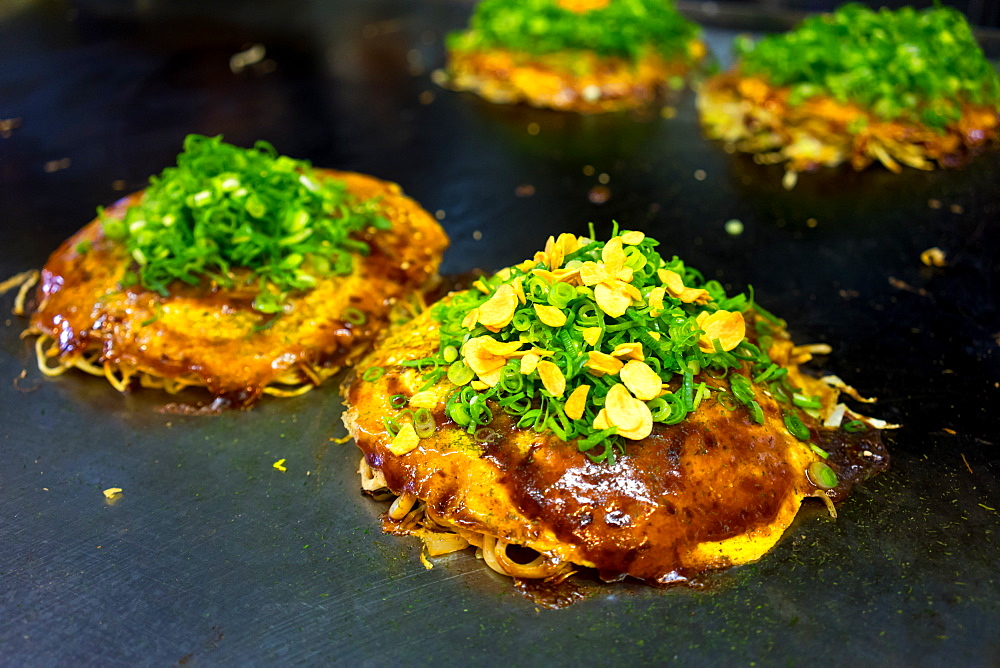 Okonomiyaki, Japanese style savoury pancakes, on a large griddle in a restaurant, Hiroshima, Japan, Asia