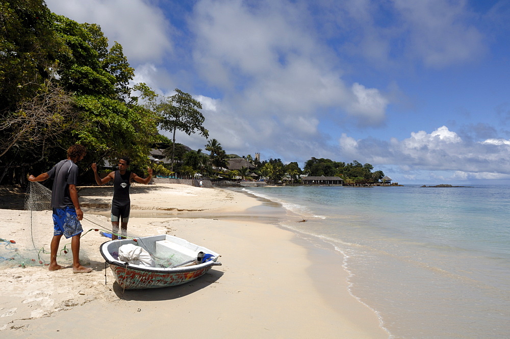 Two fishermen with boat taking fish from net on Beau Vallon beach, Mahe, Seychelles, Indian Ocean