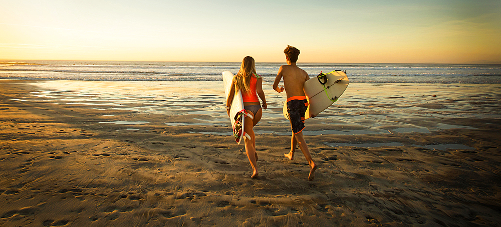 Teenage boy and girl carrying surfboards running to ocean