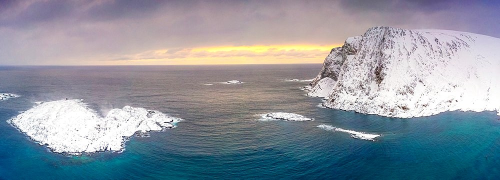 Waves of cold sea framed by snow capped mountains at dawn, aerial view, Sorvaer, Soroya Island, Hasvik, Troms og Finnmark, Arctic, Norway, Scandinavia, Europe