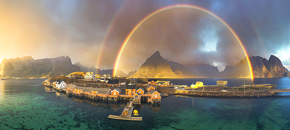 Aerial view of idyllic rainbows over Olstind mountain and fishermen cabins by the sea, Sakrisoy, Reine, Lofoten Islands, Nordland, Norway, Scandinavia, Europe