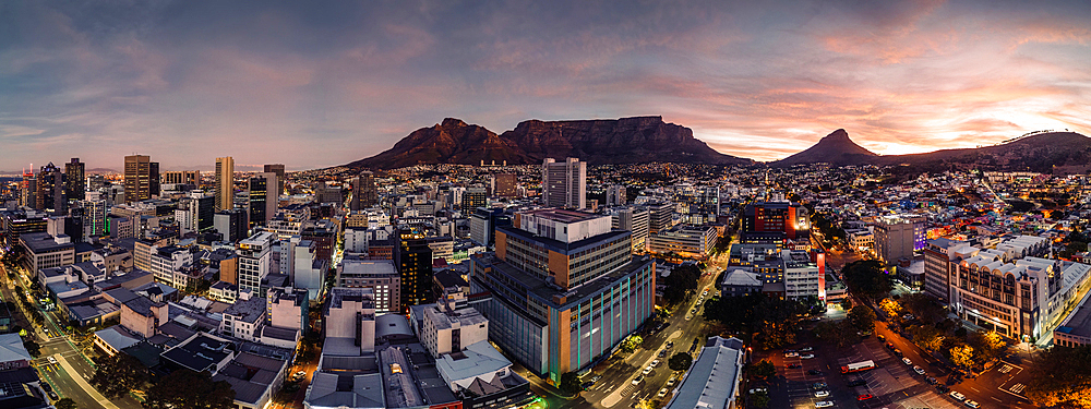 Aerial drone panoramic view of the cityscape as dusk sets in, highlighting the downtown buildings with a warm glow against the silhouette of Table Mountain and Lion's Head, Cape Town, Western Cape, South Africa, Africa