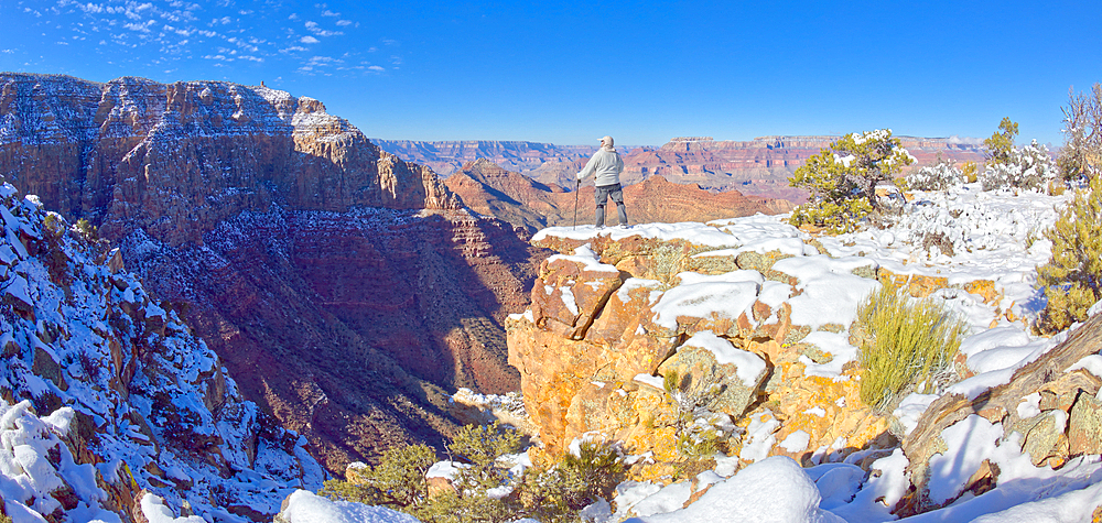 A hiker standing on a snowy cliff on the east rim of Grand Canyon National Park Arizona.