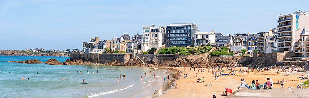 : A wide panoramic view of Rochebonne Beach in Brittany, France, filled with sunbathers and swimmers enjoying the summer sun.