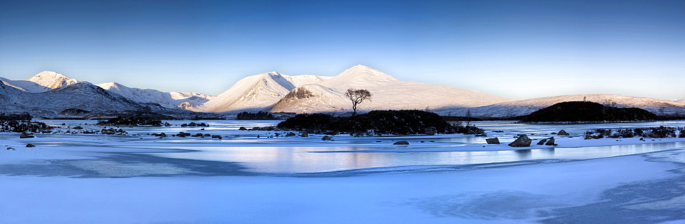 Winter view at dawn over frozen Lochain Na h'Achlaise to sun-kissed Black Mount hills, Rannoch Moor, Highland, Scotland, United Kingdom, Europe