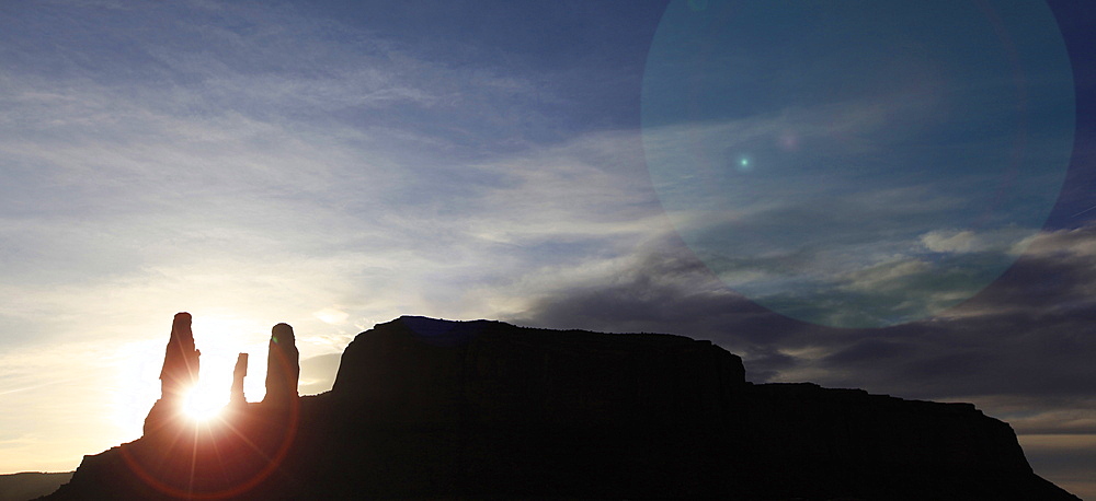 The evening sun sinks between a triple-monolith in the sandstone cliffs and pinnacles at Monument Valley, Arizona, United States of America, North America