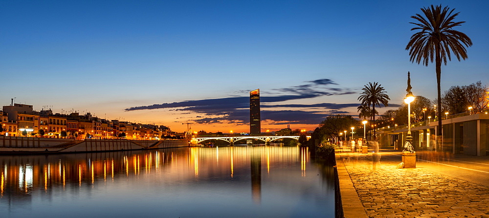 View over the river Rio Guadalquivir with illuminated bridge Puente de Triana and promenade, in the back skyscraper Torre Sevilla, sunset, blue hour, Sevilla, Andalusia, Spain, Europe