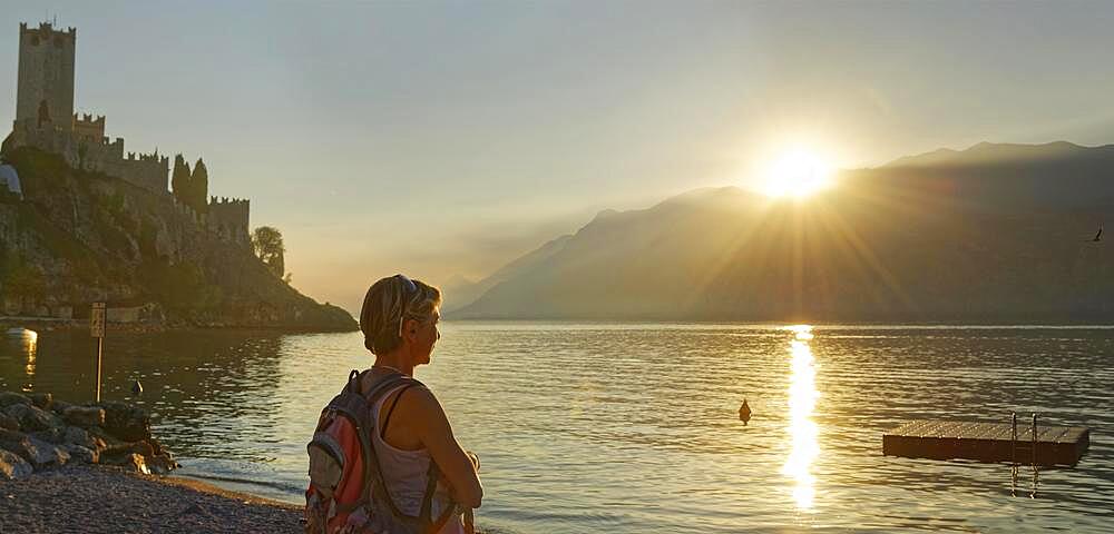 Hiker on the shore in front of Castello Scaligero at sunset, Malcesine, Eastern Lake Garda, Verona Italy, Trentino-Alto Adige, Italy, Europe