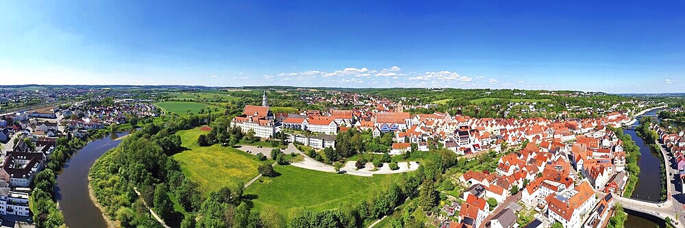 Fascinating aerial view of Donauwörth with its characteristic red roofs and historic buildings. A striking building with a tower stands out in the foreground, surrounded by well-tended green spaces and trees. The town stretches along the rolling hills and offers a picturesque atmosphere with idyllic streets, a historic townscape and expansive landscapes. Donauwörth, Swabia, Bavaria, Germany