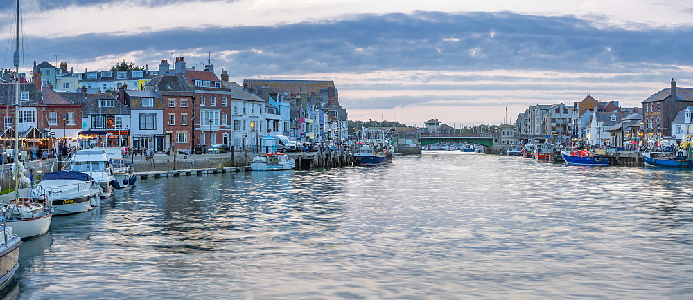 View of boats in the Old Harbour and quayside houses at dusk, Weymouth, Dorset, England, United Kingdom, Europe