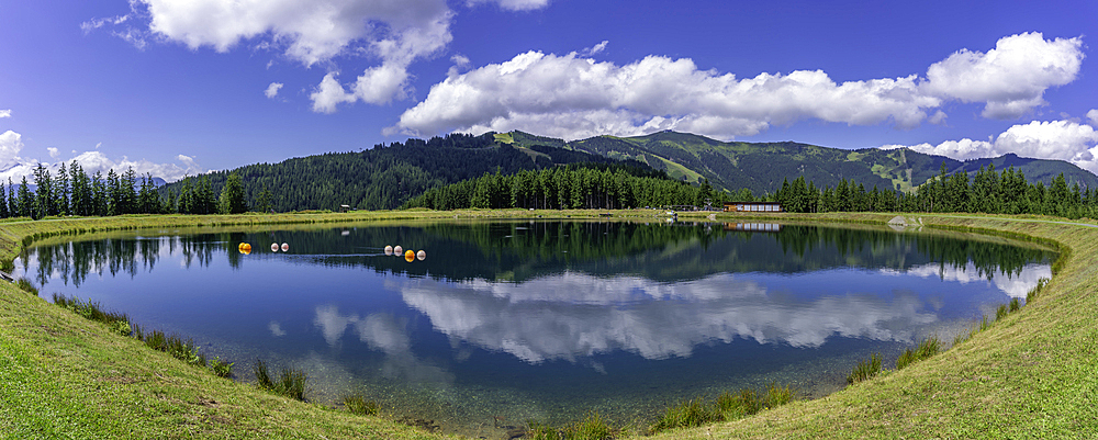 View of reflection of mountains and clouds in Plettsaukopf Reservoir on a sunny day, Bruckberg, Salzburg, Austria, Europe