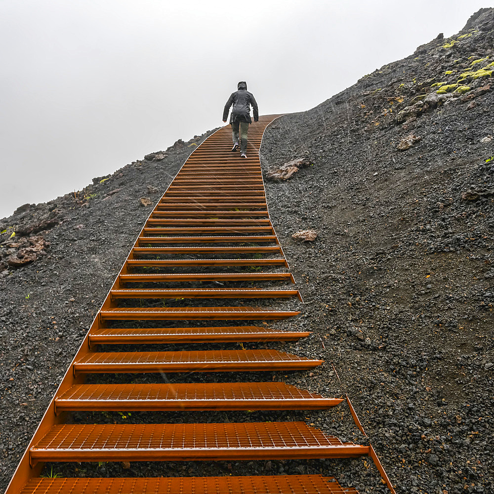 Climbing metal steps up volcanic rock in the rain; Snaefellsbaer, Western Region, Iceland