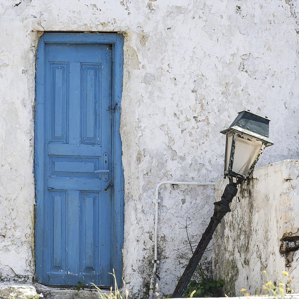 Broken lamp post beside a blue door on a dirty whitewash house in Greece, Ano Mera, South Aegean, Greece