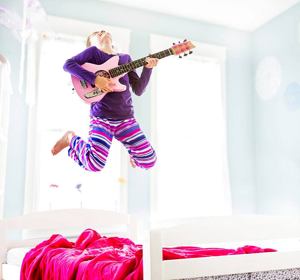 Caucasian girl playing guitar on bed