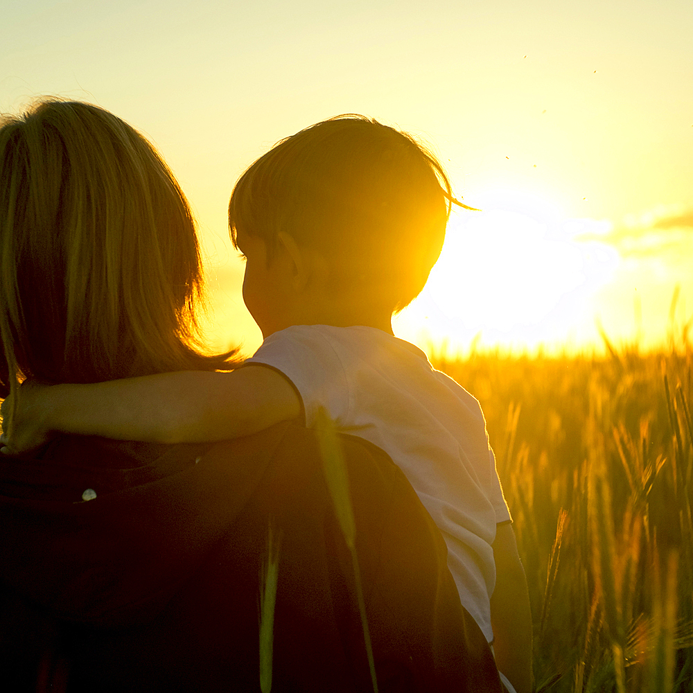 Mother carrying son in field of wheat at sunset