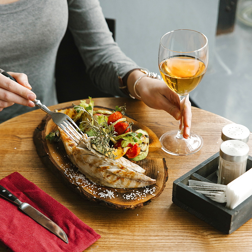 Woman eating fish with white wine