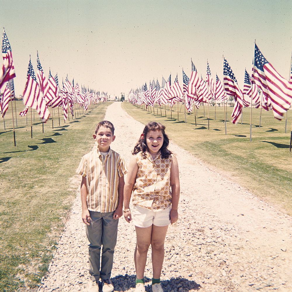 Caucasian brother and sister holding hands near American flags