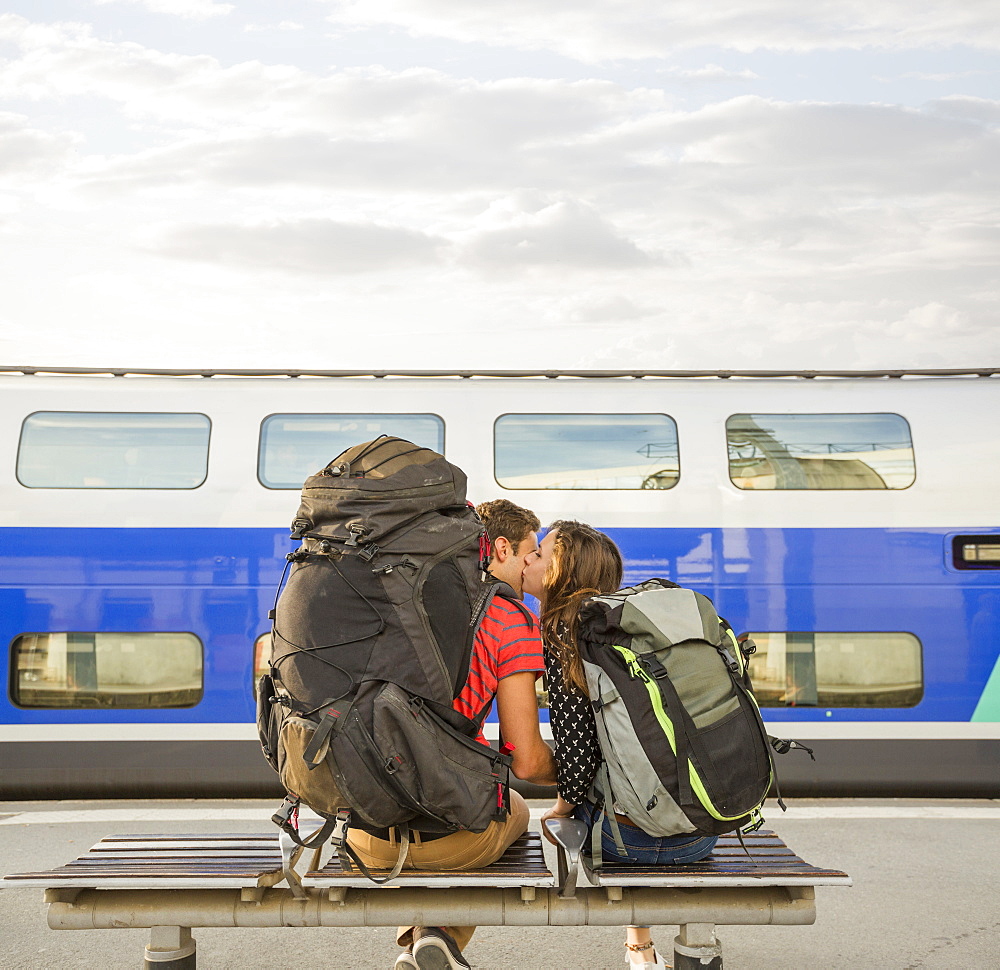 Caucasian couple kissing on bench near train