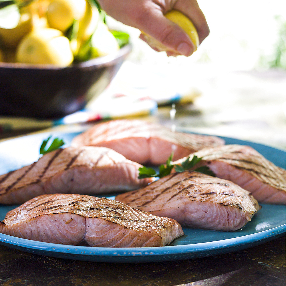 Hand squeezing juice from lemon onto plate of salmon