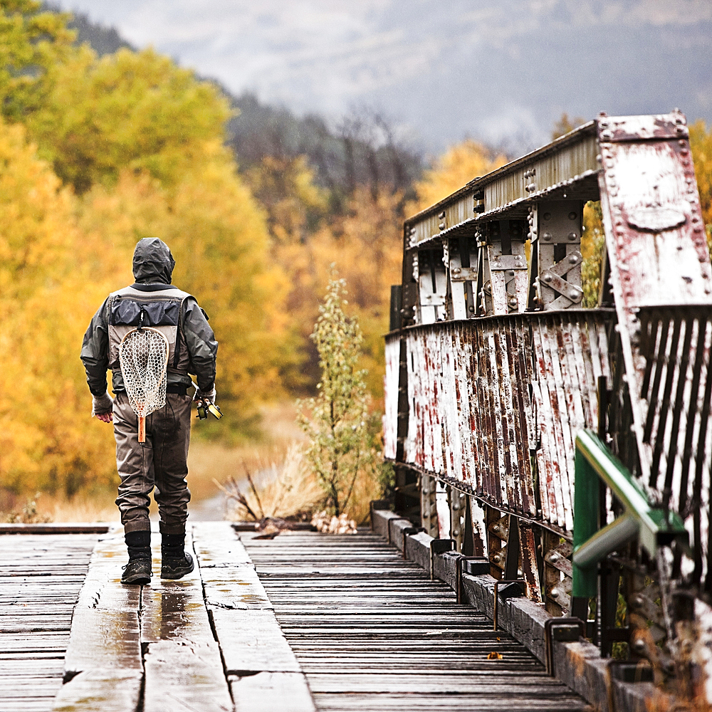 Caucasian man carrying fishing rod on bridge