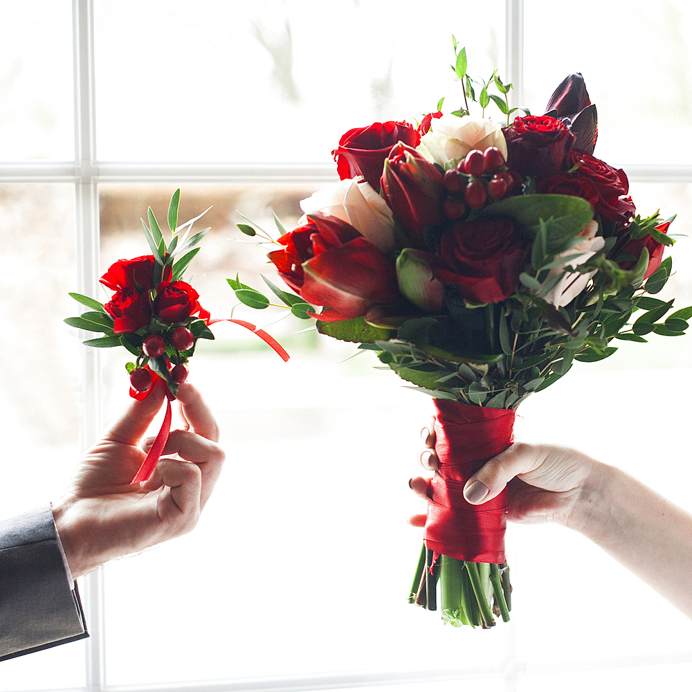 Hands of Caucasian couple holding corsage and bouquet of flowers