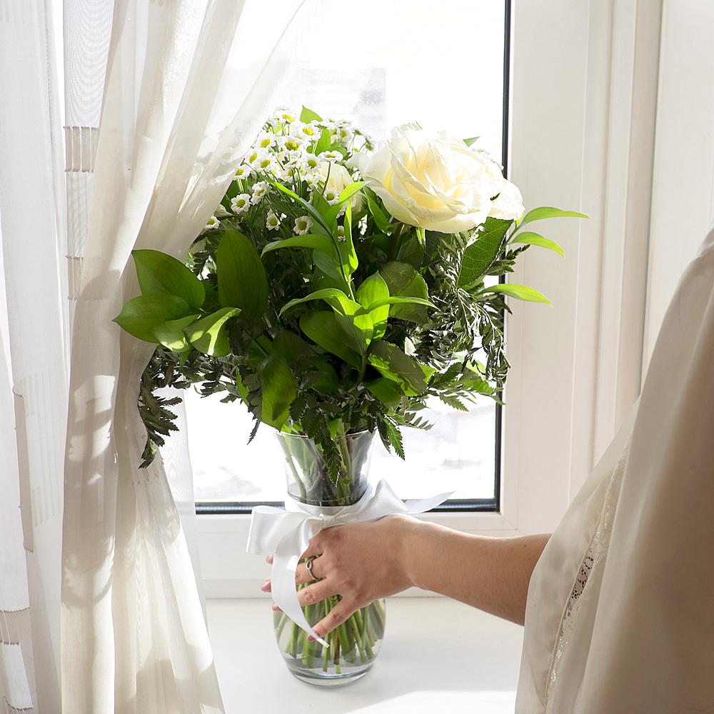 Caucasian woman placing vase of flowers on window sill